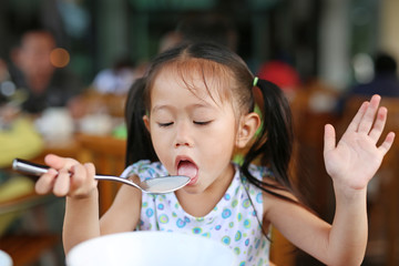 Cute asian girl eating porridge with spoon. Child eating breakfast.