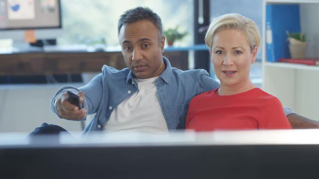 Cheerful mixed ethnicity couple watching TV and disagreeing about what to watch