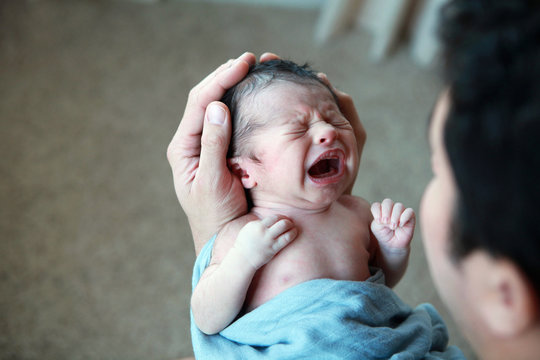 New dad holding multiethnic newborn while baby is crying
