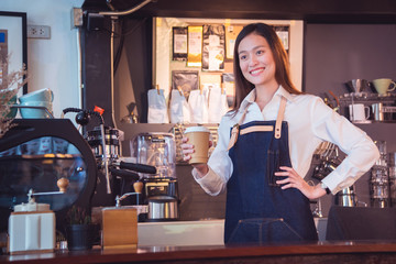Beautiful asian barista holding coffee cup and smiles in her cafe