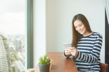 Beautiful asian woman reading message on mobile phone and smiles