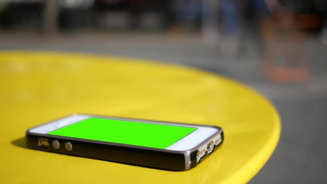 Smartphone with green screen lying on table in downtown metropolitan area on table