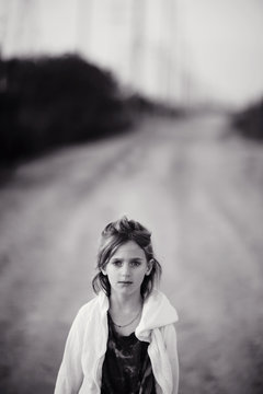 Lone girl standing on a dirt road by herself with serious expression