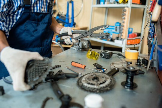 Close-up shot of unrecognizable mechanic wearing overall and checked shirt standing at desk covered with working tools and bicycle details