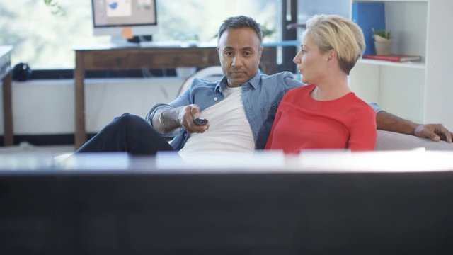 Cheerful mixed ethnicity couple watching TV and channel surfing