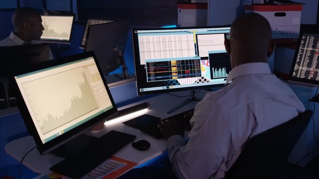  Computer expert working in a dark room surrounded by computer screens