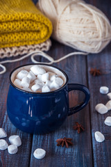 Hot chocolate or cacao in a blue mug with marshmallows on the table with wool