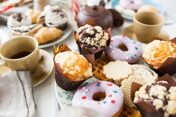 Fresh donuts, cookies and muffins on served table with cups of tea near by