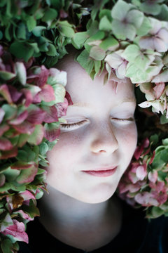 A beautiful child with her eyes closed and her face surrounded by Hydrangea flowers.
