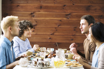 Young friendly people sitting by festive table, having talk by dessert and relaxing