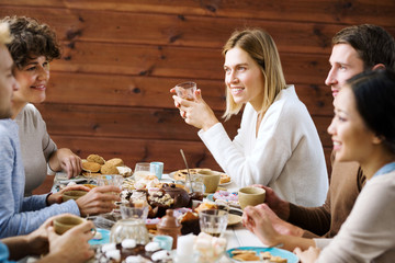 Friendly young people gathered by festive table served with homemade pastry and tea