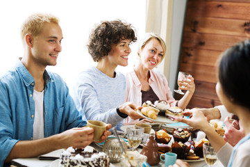 Company of happy friends having homemade dessert with drinks and talking by table