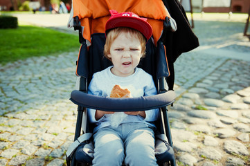 Angry little boy eating cookies in the stroller. The crisis of three years.