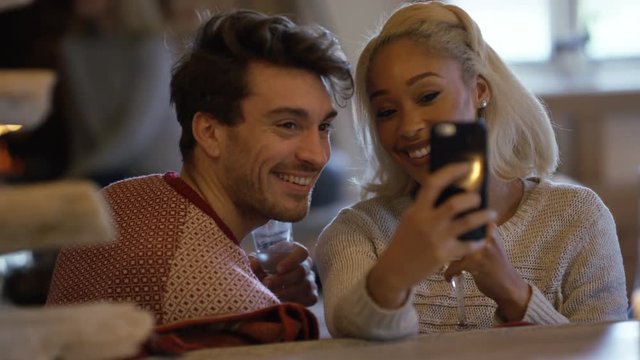  Happy couple relaxing in front of open fire, pose to take selfie with phone	