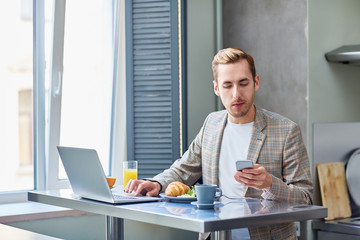 Home office worker sitting by table, texting and networking by lunch or breakfast