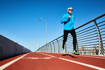 Low angle view of concentrated senior sportsman jogging outdoors and enjoying sunny warm day, full length portrait