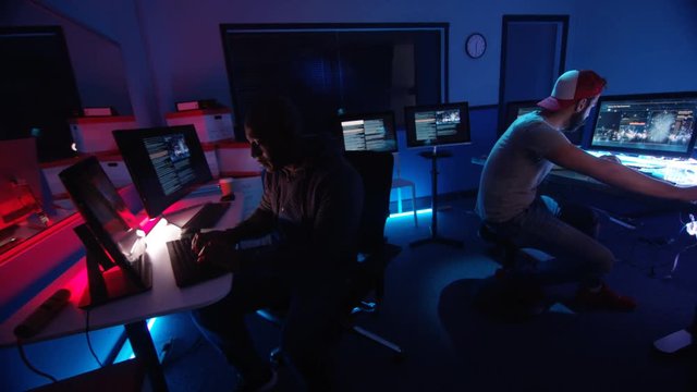  2 computer hackers surrounded by computer screens trying to break a code. Sho
