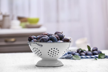 Tasty ripe plums in colander on table