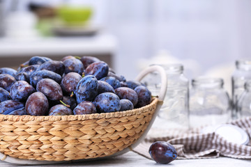 Wicker basket with tasty ripe plums on table