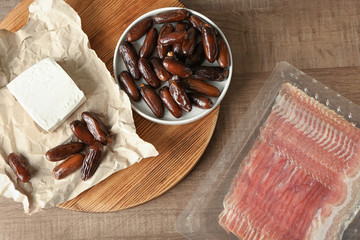 Composition with ripe dates, goat cheese and raw bacon strips on wooden background