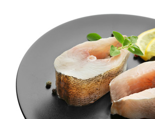 Plate with fresh fish steaks on white background