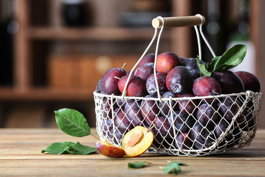 Fresh plums in metal basket on table