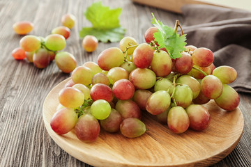 Wooden plate with ripe grapes on table