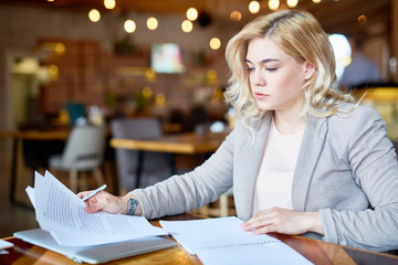 Waist-up portrait of confident blond-haired entrepreneur sitting at cafe table and taking necessary notes while preparing for important negotiations with business partner