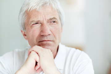 Grey-haired pensive man with his hands by chin looking aside