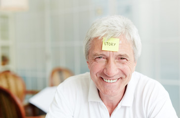 Fototapeta na wymiar Grey-haired man with notepaper on his forehead should explain or guess the word