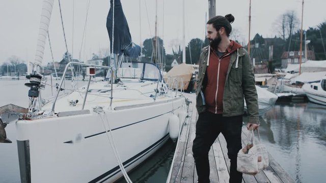 Portrait smiling bearded man standing in front of sailing boat in a marina