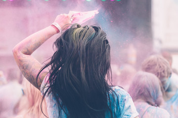 young black haired woman jumping and throwing colorful powder during outdoor concert