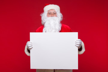 Naklejka premium Santa Claus pointing in blank advertisement banner isolated on red background with copy space