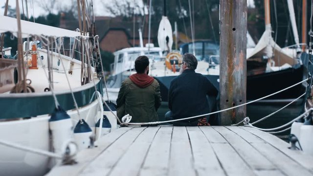  Father & son fishermen enjoying peaceful time sitting on jetty & chatting