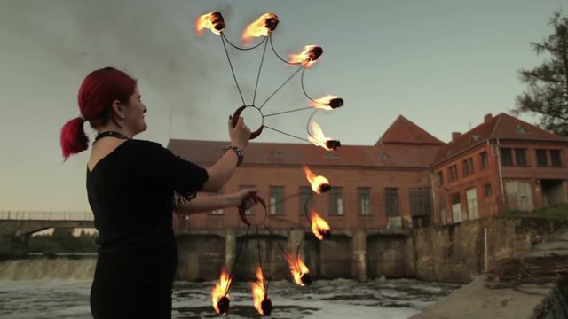 A young girl shows a fire show against the backdrop of an old German hydroelectric power station.