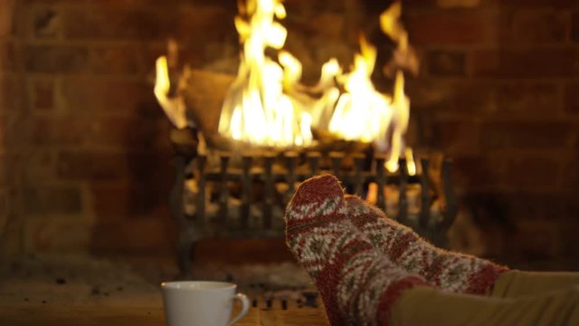 Close up feet of person in cozy socks warming their toes by the fire
