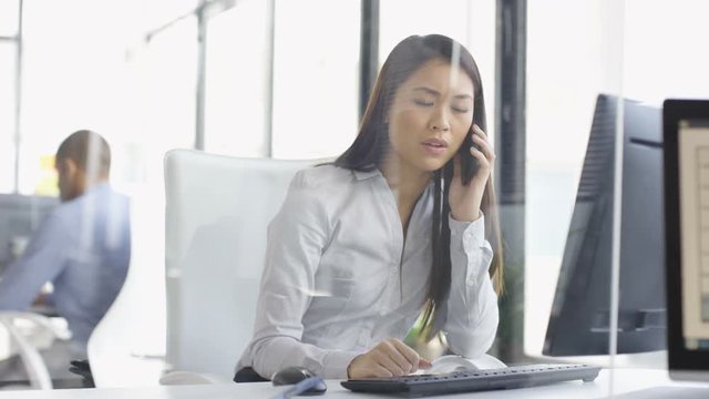  Worried businesswoman talking on phone & working on computer in office