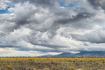 panoramic view of beautiful meadow at foot of mountains with grey storm clouds in sky
