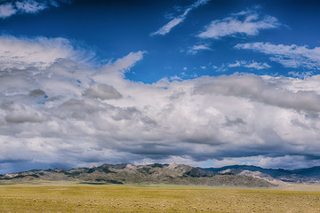 panoramic view of beautiful meadow at foot of mountains with grey storm clouds in sky
