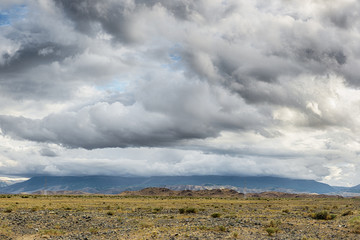 panoramic view of beautiful meadow at foot of mountains with grey storm clouds in sky

