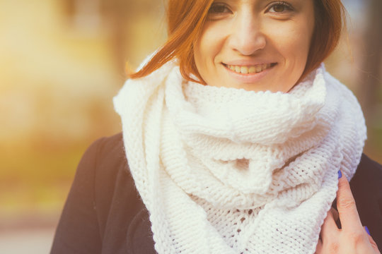 Portrait of a beautiful young woman with red hair in a large knitted white bactus scarf made of natural wool and black classic foam on a city street in the autumn day