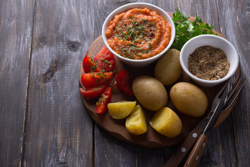 Young potatoes boiled in a peel with zucchini caviar or dip of vegetables, spices, fresh tomatoes and parsley on a wooden board, free space. Simple healthy homemade food