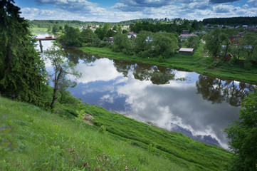 View of the blue river from a high green hill. The beauty of nature. Blue sky with clouds and green summer around.