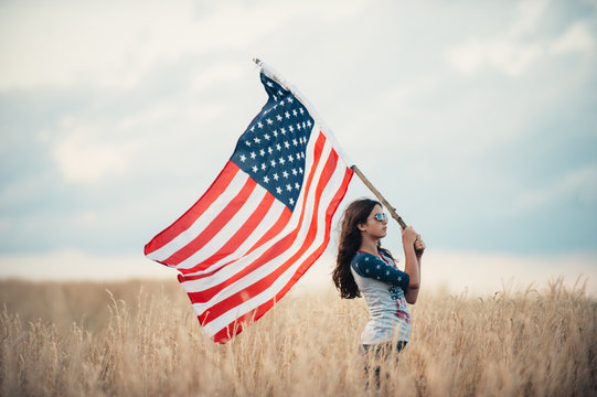 A young woman waving American flag while standing in a field