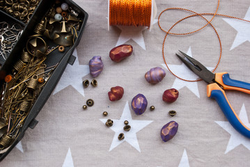 Assembly of jewelry of polymer clay in bohemian style with gold elements and box with small beads. Hobby, handicraft. Pilers with unfinished necklace.Trend color bordo.