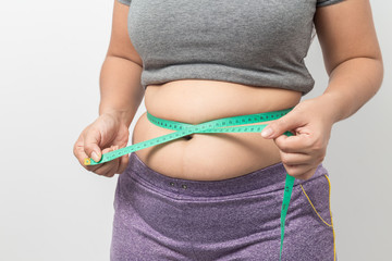 Overweight woman check out his body fat with green measuring tape for obesity on gray background,...