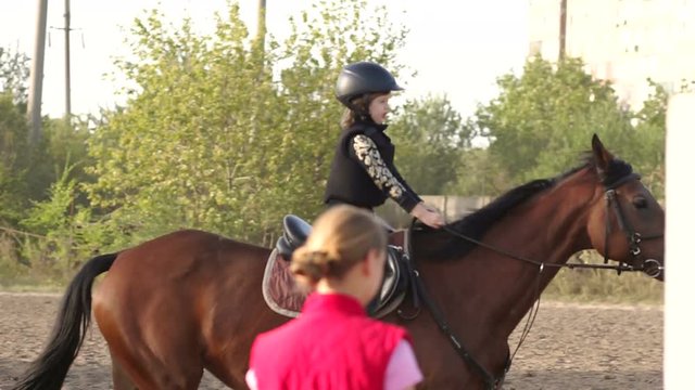 Little girl of 4-5 years in a helmet is engaged in riding a horse farm at sunset in autumn. Slow motion.