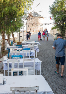 Unidentified People walk at a street with cafe and restaurant with tables and chairs  around at Alacati Town,a popular destination for traveling and vacation in Izmir,Turkey.26 August 2017.