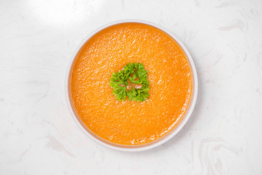 Carrot soup with cream and parsley on white stone background. Top view. Copy space