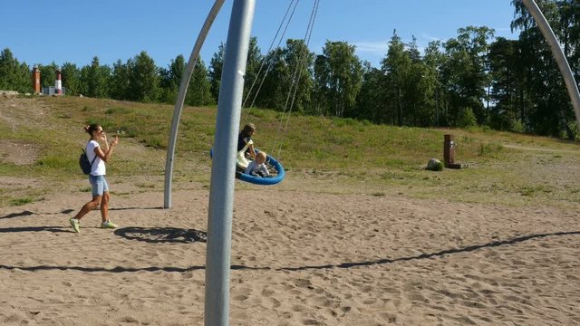 Mom with two little girls walking in park and swinging on big swing set